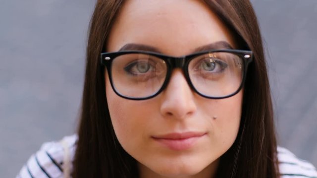 Beautiful young woman looking down and straight at the camera and smiling while standing outdoors inh the street. Close up