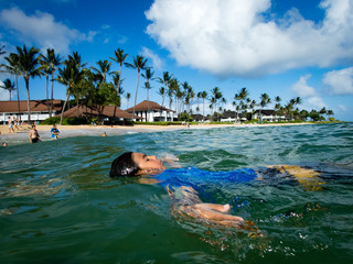 10 year old boy floating on back ain ocean at resort, Kiahuna Beach, Poipu Beach in front of...