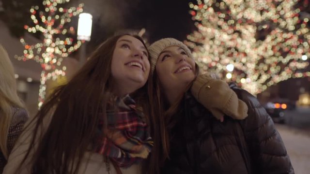 Closeup Of Friends Walking, Enjoying Christmas Lights, They Look Up Together And Laugh And Smile