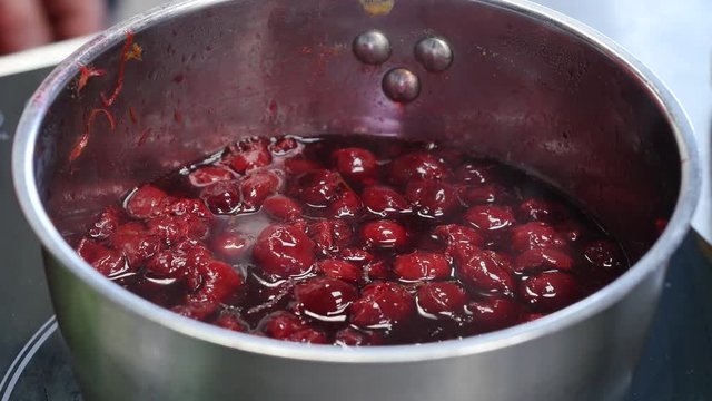 Closeup stirring cherry jam with spoon in metal saucepan. Close up of simmering homemade cherry jam. Cooking Homemade Cherry Jam
