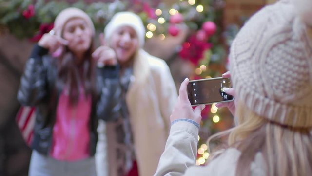 Two Girls Pose For Photos In Front Of Christmas Decor At Mall, Friend Snaps Pics With Smart Phone 