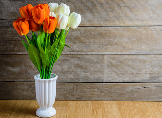 orange, white tulip flowers bouquet in vase on wooden floor
