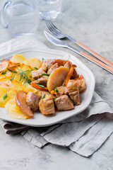 Pork stewed with apples with potatoes for garnish on plate on gray table background. Meat for lunch/dinner