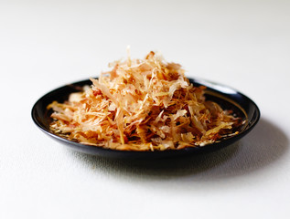 Closeup of katsuo bushi (fish flakes) on a dark plate against a white background (low angle closeup)