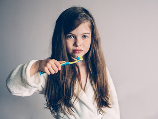 Little cute girl in a bathrobe brushing her teeth