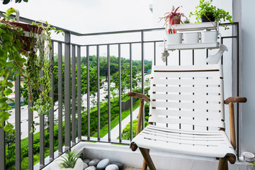 Outdoor chair sits on a balcony inside condominium. The railing is a fence design with vertical thin metal louvers. Planters were places all around and also pebbles on the floor.