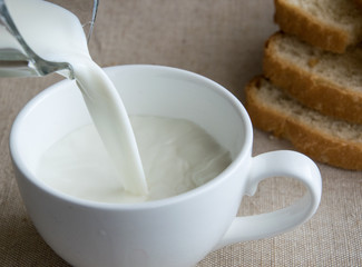 Pouring milk into a large white cup on the background of bread.