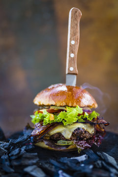 Tasty smoked grilled and glazed beef burger with lettuce, cheese and bacon served on wooden table with copyspace, smoke mesquite timber wood in background.