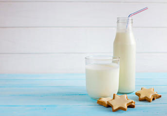 Milk in a glass bottle and in a glass with a biscuit asterisks on a blue wooden background