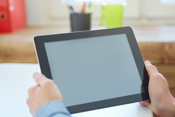 Man's hands holding tablet computer closeup on a light wooden table. Concept man working in the morning from home using tablet computer.