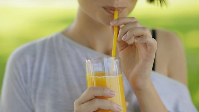 Healthy lifestyle food. Young woman drinking fresh orange juice outdoors at summer park in slow motion