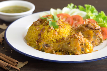 Chicken Biryani on white dish with green sauce (Muslim yellow rice with chicken) on brown wooden background..