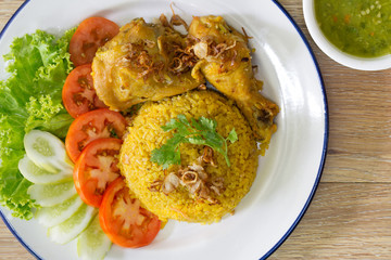 Chicken Biryani on white dish with green sauce (Muslim yellow rice with chicken) on brown wooden background.