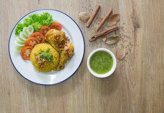 Chicken Biryani on white dish with green sauce (Muslim yellow rice with chicken) on brown wooden background.