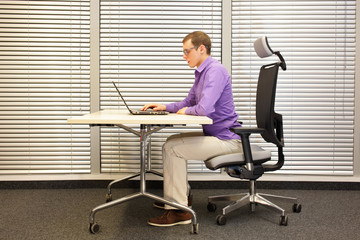  sitting position at workstation. man on chair working with laptop