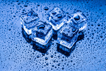 Wet ice cubes and water drop on blue background.