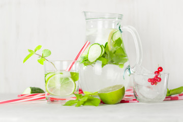 Detox water in a glass jug and a glass. Berries and lime, red and green. Fresh mint leaves.