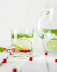 Detox water in a glass jug and a glass. Berries and lime, red and green. Fresh mint leaves.