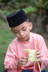 Fototapeta premium Muslim boy in malay traditional cloth is filling the rice into the ketupat clad 