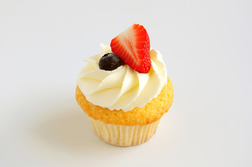 Cupcake with whipped cream, fresh strawberry, blueberry on white background. Picture for a menu or a confectionery catalog.