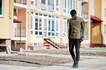 Handsome and attractive african american man in sunglasses posing next to the tall building on a street.