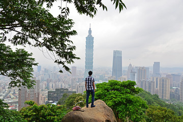 101 tower and city of Taipei with a young man figure viewed from behind.
