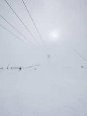 Skiers in thick fog on ski slope in ski resort.
