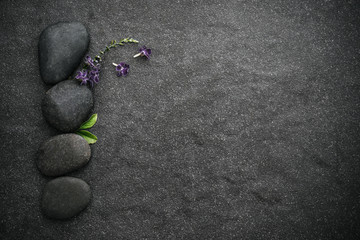 the black stone with green leaf and small cute purple flower decoration on stone plate background with copy space for spa and meditation concept background