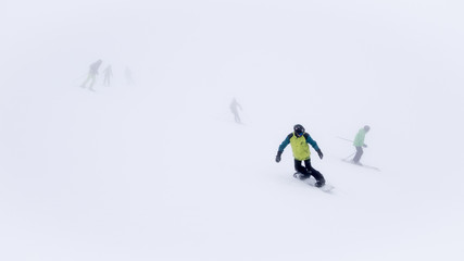 Skiers and snowboarders in thick fog on ski slope in ski resort.