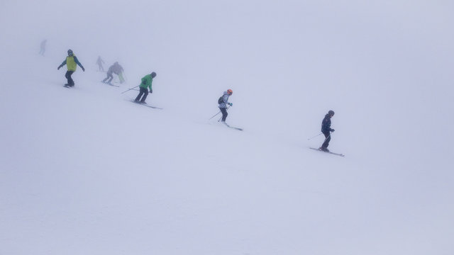 Skiers and snowboarders in thick fog on ski slope in ski resort.