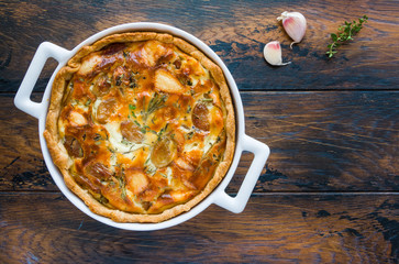 Quiche-like caramelized garlic tart with rosemary and thyme in a white pan on the wooden rustic table, top view.