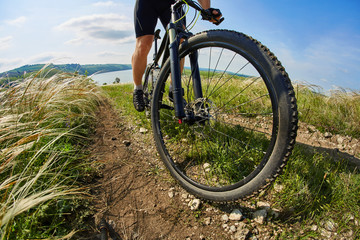 Fototapeta na wymiar Young cyclist riding mountain bicycle through green meadow against beautiful sky.