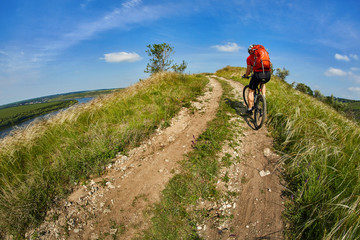 Young cyclist riding mountain bicycle through green meadow against beautiful sky.