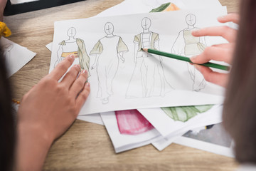 cropped shot of fashion designers working with blueprints of models