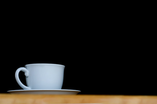 A white cup of coffee in the dark background on wood table.