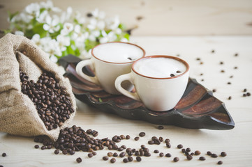 Two cups of freshly brewed, frothy cappuccino. Spilled coffee grains, chocolate and cane sugar. Theme of coffee, cappuccino, mocha chino, america no. Beautiful elegant background with place for text
