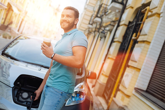 Young Man Charging His Car And Drinking Coffee