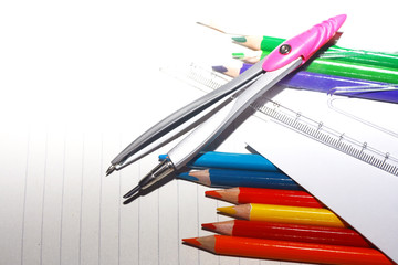 Photo of crayons with ruler and compass on exercise book and a paper