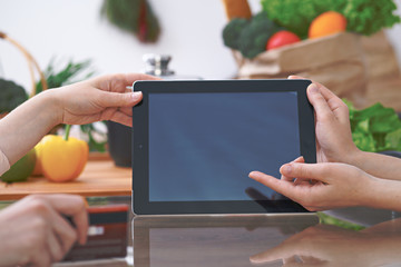 Close-up of four human hands are gesticulate over a tablet in the kitchen. Friends having fun while choosing menu or making online shopping. So much ideas for tasty cooking. 
