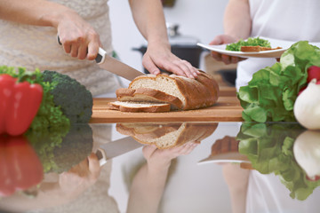 Close-up of human hands slicing bread in a kitchen. Friends having fun while preparing fresh salad. Chef cook represent culinary masterclass. Vegetarian, healthy meal and friendship concept