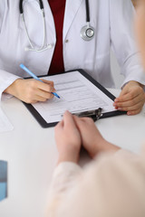 Fototapeta premium Close up of a female doctor filling up an application form while consulting patient