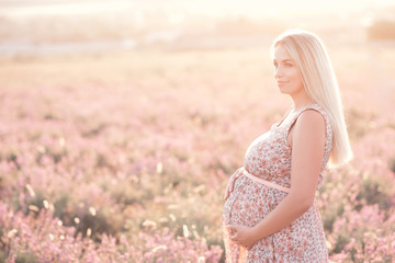 Fototapeta na wymiar Smiling pregnant woman 25-29 year old resting in lavender field. Posing outdoors. Motherhood. Maternity. 20s.