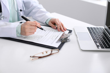 Close-up of a female doctor filling  out application form , sitting at the table in the hospital