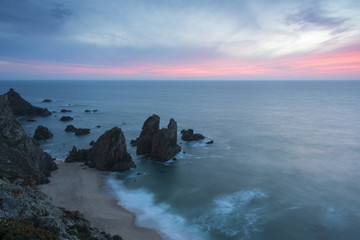 Portuguese coast with stones in the ocean and beautiful pink sunset