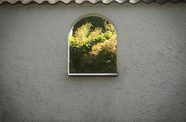 Beautiful summer season specific photograph. White concrete wall with nice textures and character and cut out window showing beautiful nature/vegetation/plant scene. - 163013530