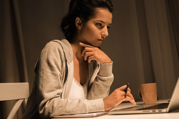 young pensive woman working on laptop while sitting at home