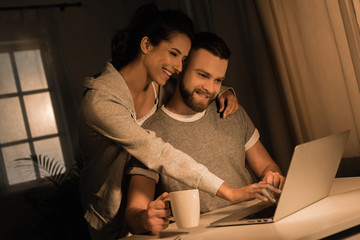 young smiling couple embracing while using laptop at home