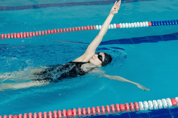 Young girl in goggles and cap swimming backstroke
