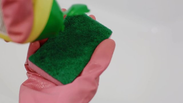A woman in pink rubber gloves pours a cleanser on a sponge. Closeup shot.
