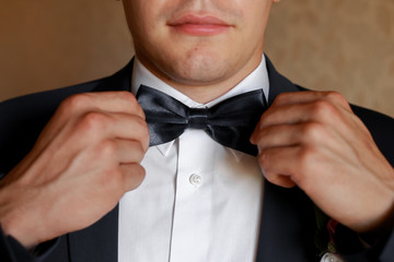 groom correct his butterfly in black suit. Photo of a male butterfly close-up